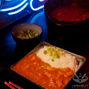 Food photo with a futuristic Cyberpunk style. A plate of Japanese curry and rice, with some scallions and a pot of leftover curry in the background.