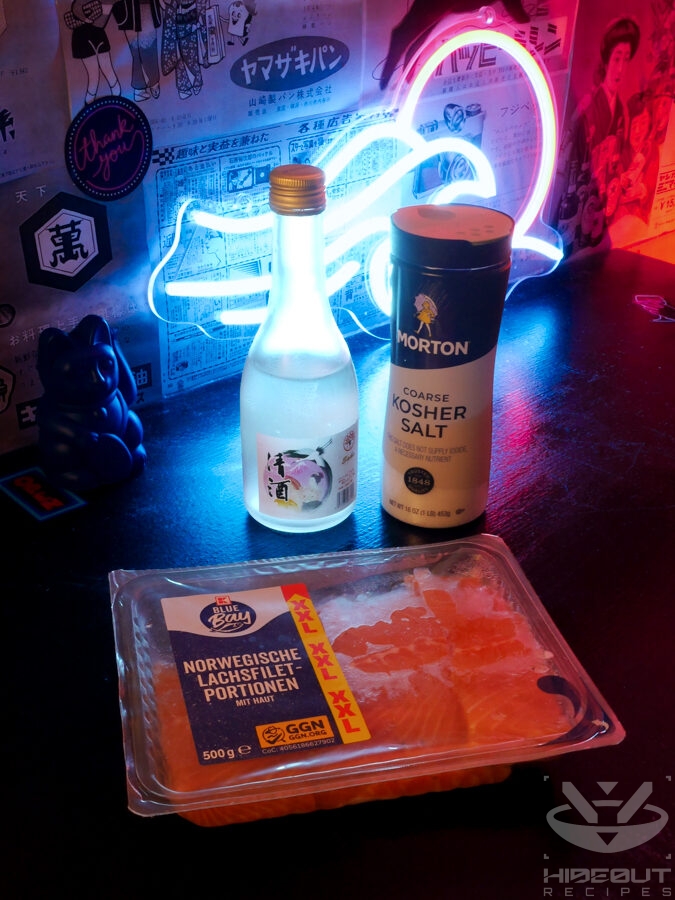 A pack of salmon with a shaker of kosher salt and a bottle of sake in the back.