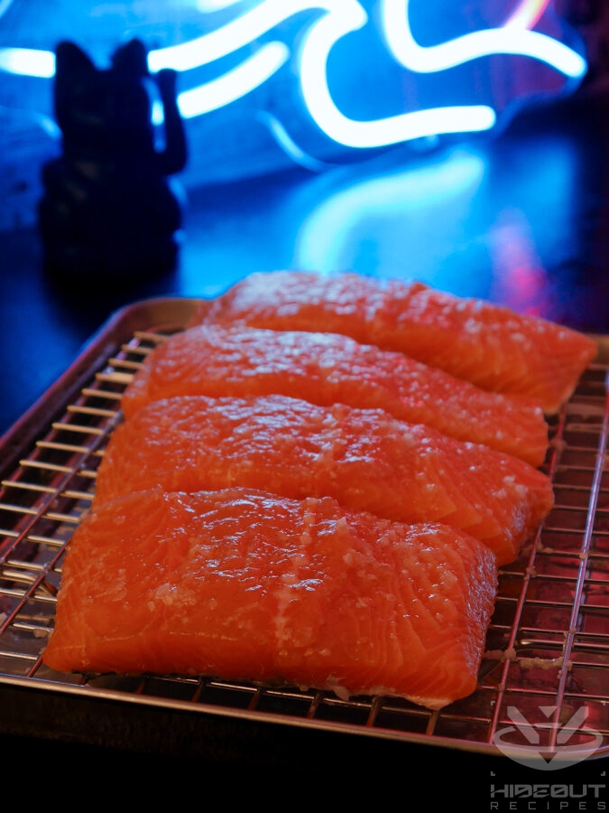 Four salmon fillets on a metal rack over a drip pan are covered in sake and kosher salt.
