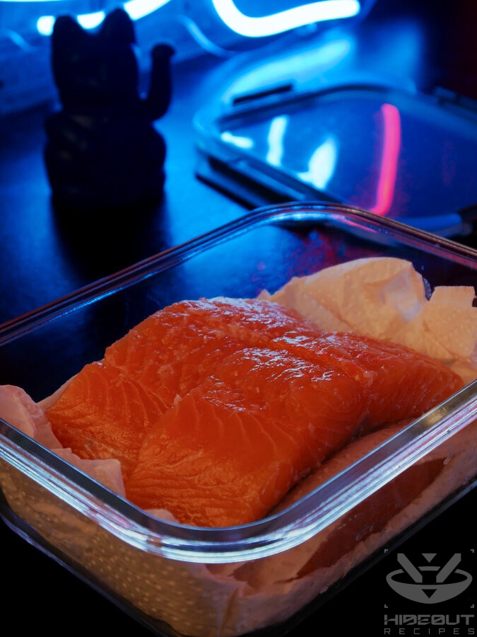 Four salmon fillets covered in sake and kosher salt are placed inside a glass Tupperware container padded with paper towels.