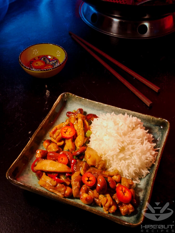 A plate of Thai Cashew Chicken with rice. Chopsticks and additional slices of red chilies can be seen in the background.