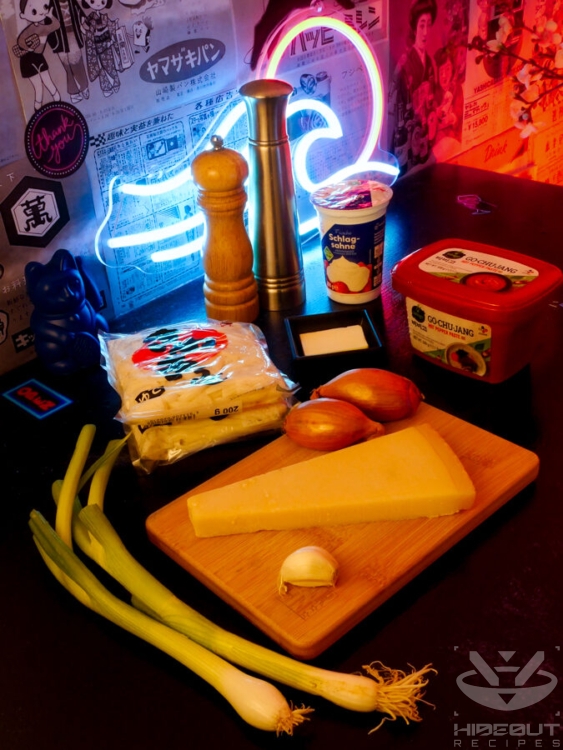 Ingredients for Gochujang Udon in their packaging are distributed across a table, a large piece of parmesan at the center.