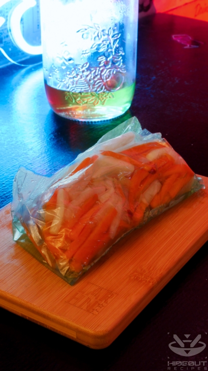 Julienned carrots and radish are pickled inside a freezer bag, with some leftover liquid in a jar in the back.