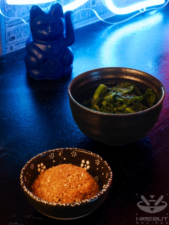 A bowl of cooked spinach and of pre-mixed sesame seasoning are placed on the table in two small bowls.