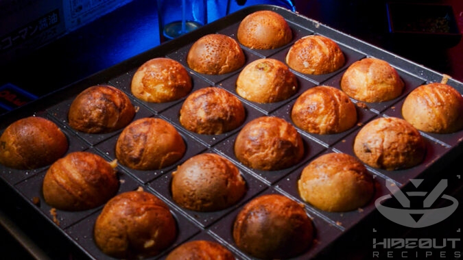 A close-up of Takoyaki being made on a small specialized gas-powered grill.