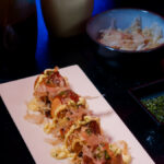 Some Takoyaki on a plate, topped with Aonori, Katsuobushi, Okonomi Sauce, and Kewpie Mayo.
