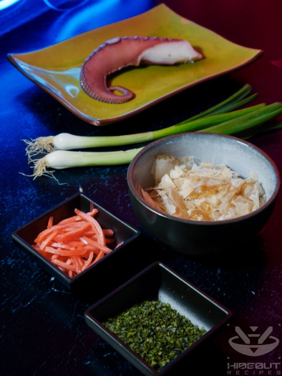 Ingredients for Takoyaki fillings and toppings are placed on a table, including a fresh octopus tentacle.