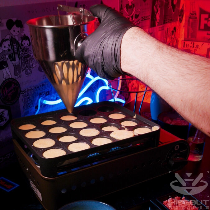 A gloved hand is using a dough dispenser to fill a Takoyaki grill with batter.