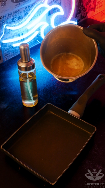 A gloved hand is about to pour some pre-mixed Tamagoyaki from a measuring cup into an oiled rectangular pan.
