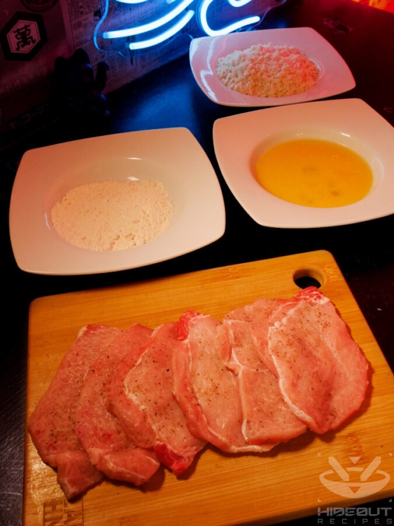 Six Tonkatsu cutlets are placed on a wooden board, surrounding by deep plates containing flour mix, eggs, and panko breading.
