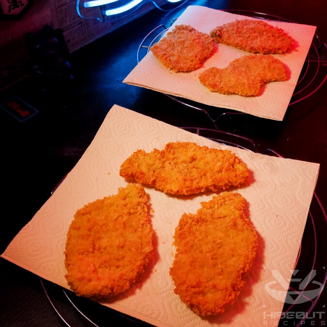Six Tonkatsu cutlets are placed on paper towels on wire racks. They have been deep-fried once and are awaiting the second go-around.