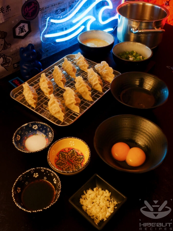 Pre-measured ingredients for Manduguk (Korean dumpling soup) are distributed to small bowls. Mandu are lying on a wire rack, and a pot of soup stock is in the background.