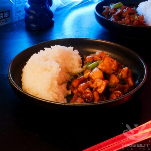 A futuristic Cyberpunk-style food photo. A plate of Ginger Chicken and rice is at the center, with glowing red chopsticks in front and another plate in the back.