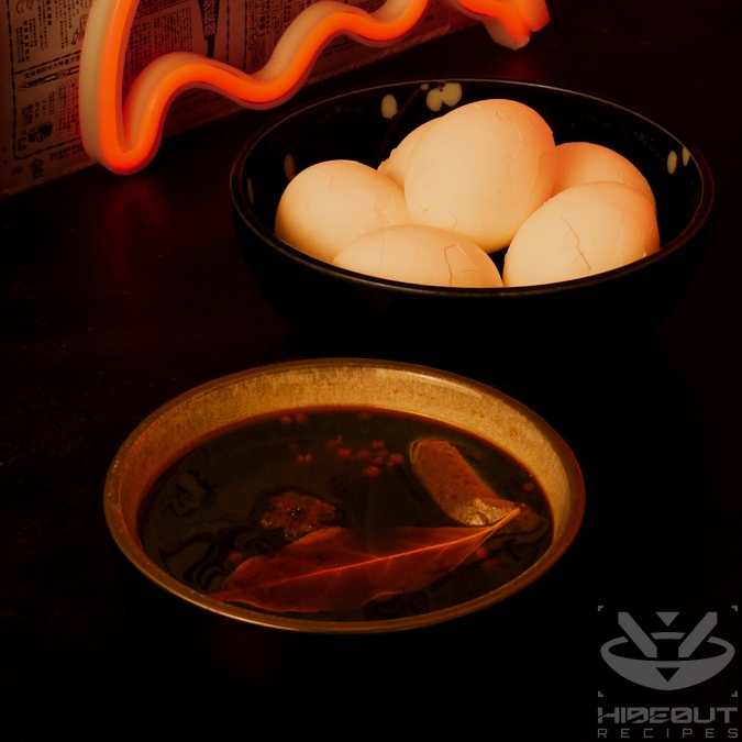 A close-up of two bowls respectively containing six eggs with cracked shells and the mixed marinade for Chinese Tea Eggs.