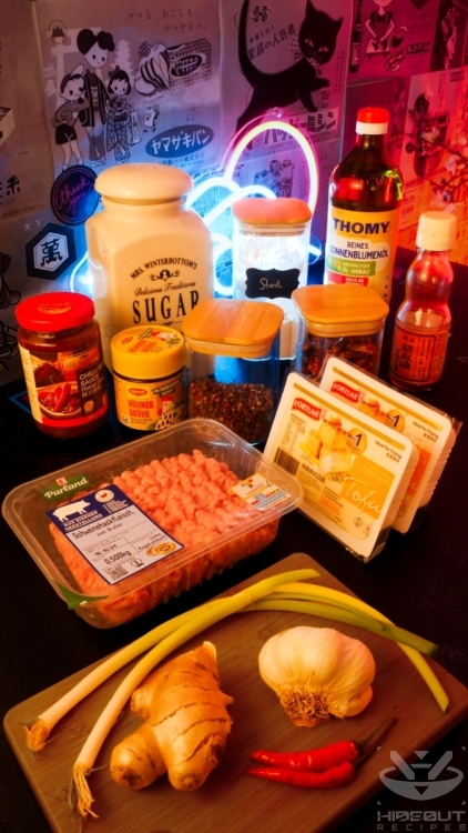 Ingredients for Mapo Tofu are gathered on a table in their packaging, with a wooden board of fresh vegetables in the foreground.