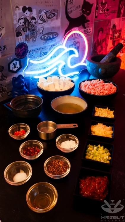 Pre-measured and prepared ingredients for Mapo Tofu are gathered on a table in countless small bowls, with a large pestle and mortar in the background.