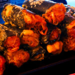 A futuristic Cyberpunk-style food photo. Spring rolls containing noodles in a spicy sauce, nori, and cheese are stacked up on a plate.