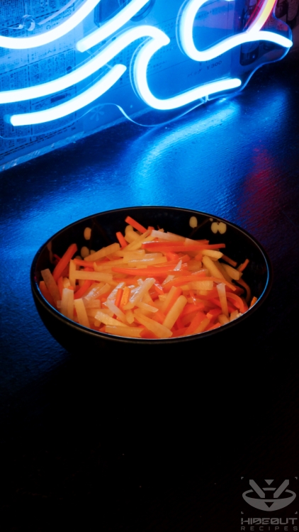 A bowl of julienned and pickled radish and carrot is standing on a table.