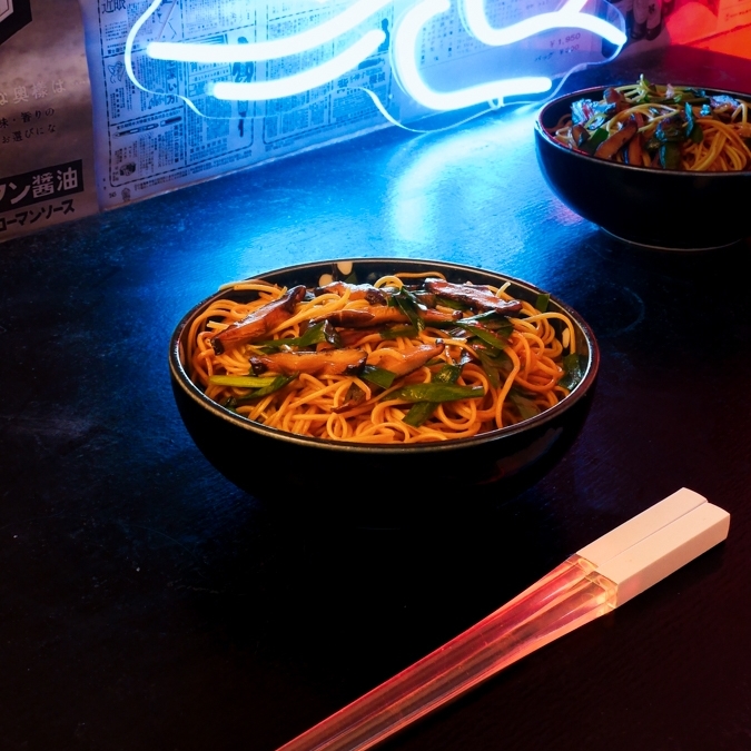 A futuristic Cyberpunk-style food photo. A bowl of Yi Mein noodle stir-fry with shiitake and Chinese chives is at the center, and a pair of red glowing chopsticks in the foreground.