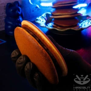 A futuristic food photo in a Cyberpunk aesthetic. A hand is holding a Dorayaki (Japanese red bean pancake) into the camera, with a stack of them in the back.