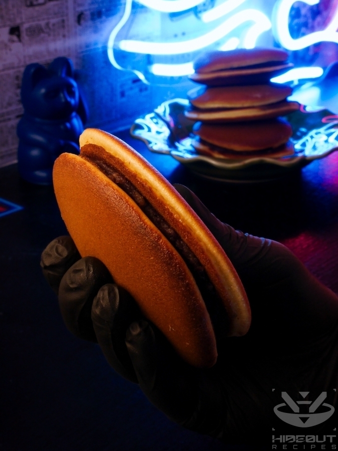 A futuristic food photo in a Cyberpunk aesthetic. A hand is holding a Dorayaki (Japanese red bean pancake) into the camera, with a stack of them in the back.