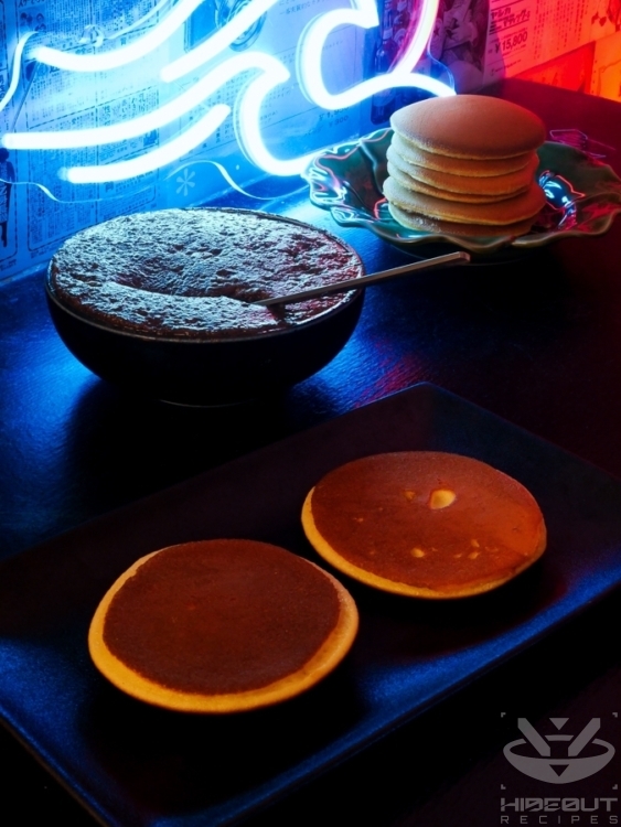 Two pancakes lie on a plate, with sweet red bean paste next to it ready to be applied with a spoon.