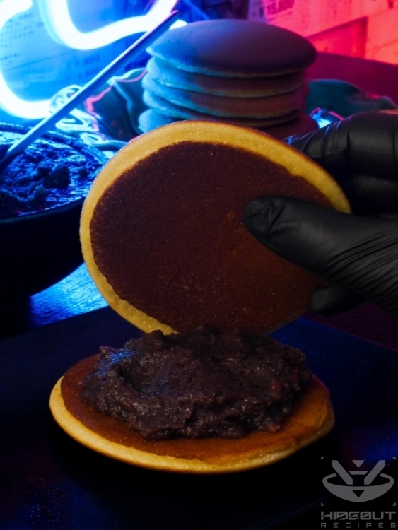 A hand moves a Dorayaki pancake onto another with red bean paste on it.