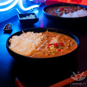 A futuristic Cyberpunk-style food photo showing a plate of Thai Red Curry and Jasmine rice, surrounded by small bowls of toppings and a large wooden spoon.